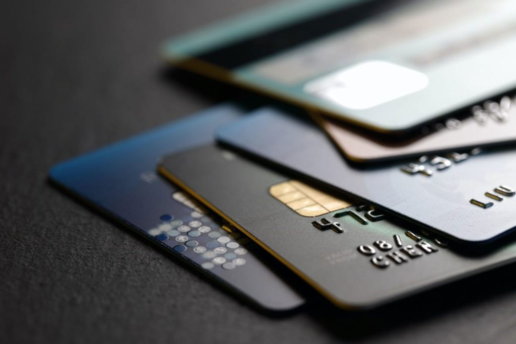 The image displays a collection of credit cards and debit cards laid out on a dark surface, with each card showing different designs and numbers on their fronts.