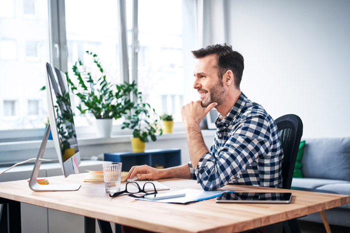 The image shows a man sitting at a desk with his hand on his chin, appearing to be deep in thought or contemplation.