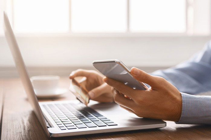 A person s hands using a laptop computer while sitting at a table with a cell phone nearby.